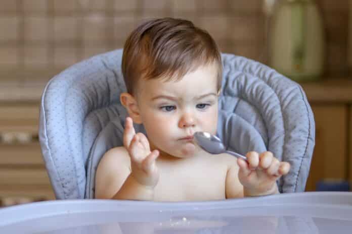 Cute little baby boy looking at spoon in his hand with funny bewildered face expression thinking what to do with it BABY FOOD METALLI PESANTI