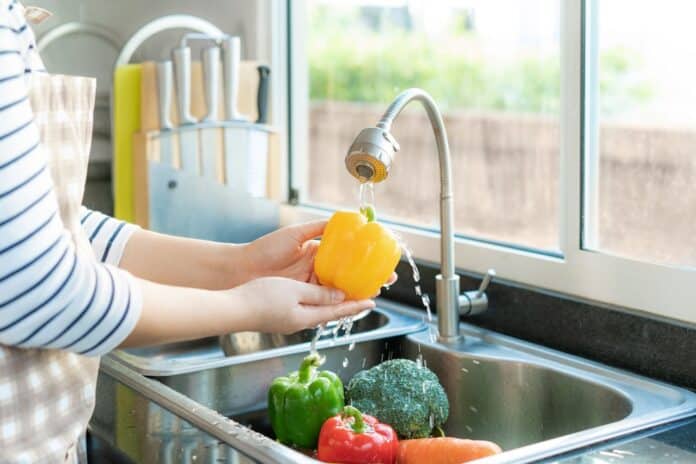 Asian healthy woman washing yellow bell pepper and other vegetable above kitchen sink and cleaning a fruit / vegetable with water to eliminate the chances of contamination COVID-19. frutta