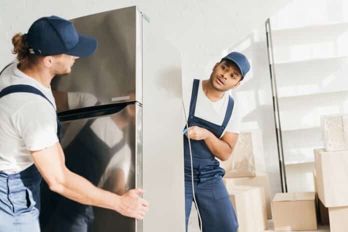 Indian mover looking at coworker while moving fridge in apartment MEDIAWORLD CONSEGNA AL PIANO