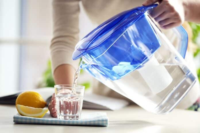 Woman pouring water from filter jug into glass in the kitchen caraffe