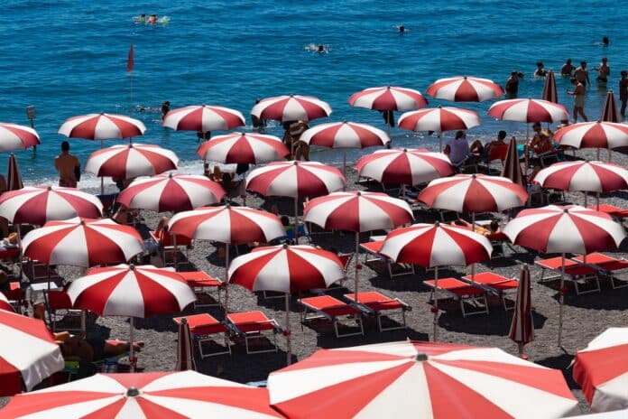 Amalfi beach on famous Amalfi Coast Italy. Rows of red and white parasols or beach umbrellas and tourists relaxing in the sun or bathing in the turquoise sea. Popular holiday destination near Naples. MARE LAZIO