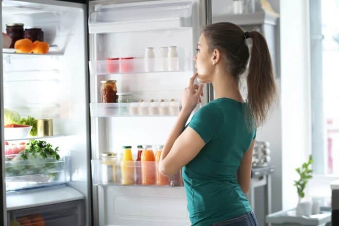 Woman standing near open fridge at home alimentare