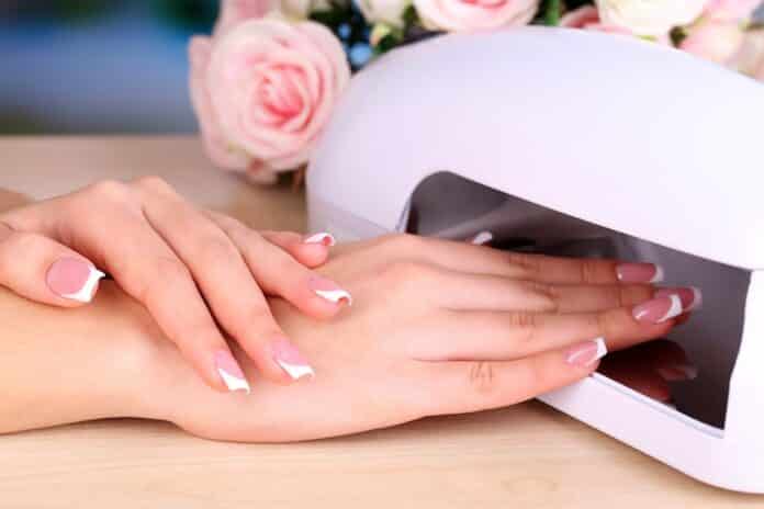 Beautiful woman hands and lamp for nails on table close up unghie
