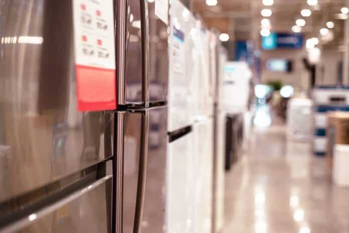 Selective focus on product tag of French door refrigerator on display at hardware store in Dallas, TX. Blurry hallway industrial ceiling lights, polished floor evokes big-box retail environment