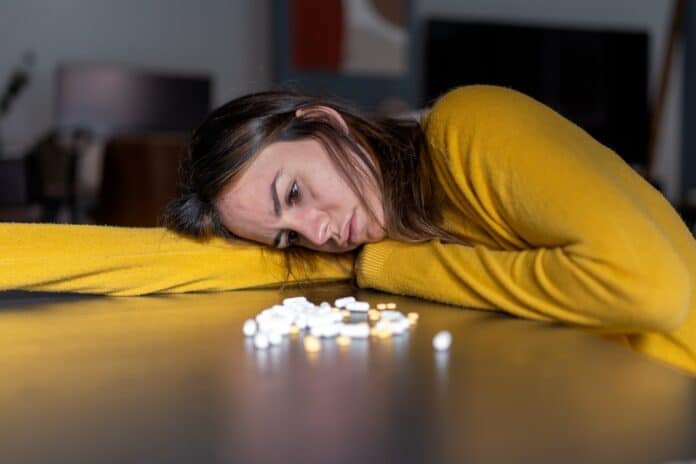 Upset woman lying on table with heap of pills SERTRALINA