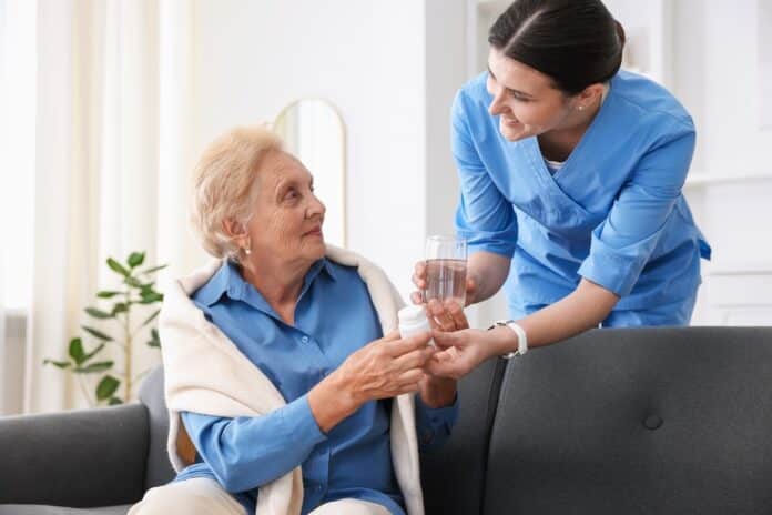 Nurse giving glass of water and pills to senior woman indoors. Home health care service assistenza