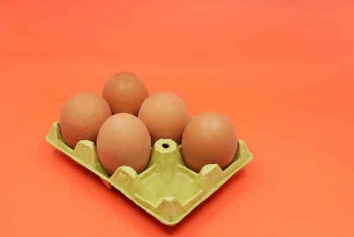 Five brown eggs instead of six in an open egg carton on orange background. Shrinkflation concept. SHRINKFLATION