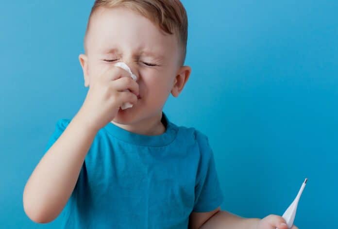 Ill young child with a thermomether, measuring the height of his fever and looking into the camera pfas