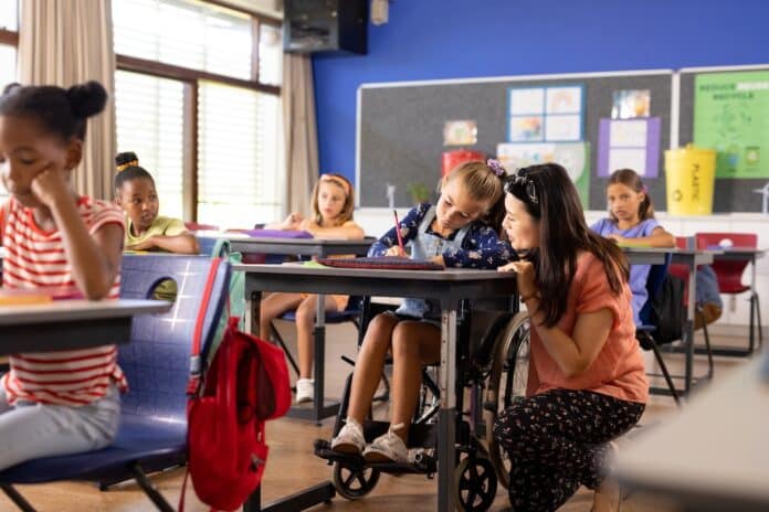 Diverse female teacher and schoolgirl in wheelchair in elementary school class sostegno