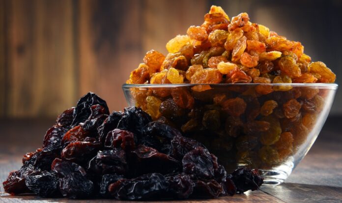 Composition with bowl of raisins on wooden table PESTICIDI UVETTA