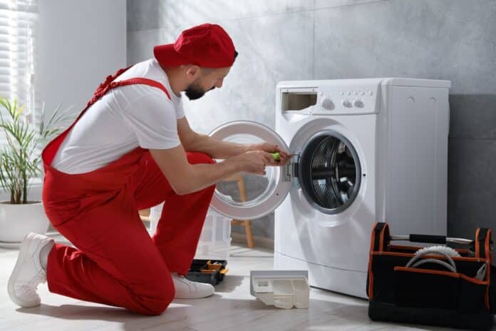 Professional repairman fixing broken washing machine indoors INDICE DI RIPARABILITA'