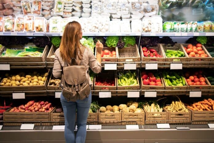 Good looking woman standing in front of vegetable shelves choosing what to buy. Buying groceries and healthy organic food in supermarket. frutta e verdura