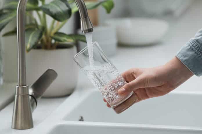 Woman filling glass with water from tap in kitchen, closeup acque