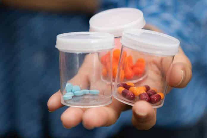 Close-up of a hand holding several small transparent containers filled with different types of pills and capsules. Concept of medication variety pfas