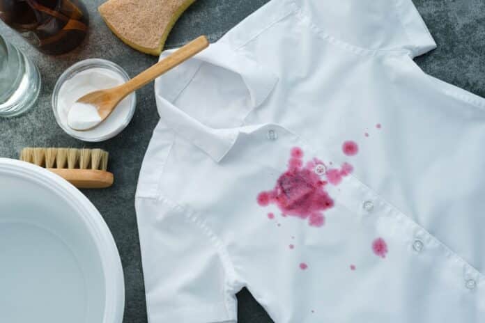 Natural cleaning ingredients baking soda, sponge, cold water, brush, vinegar. Spilled red wine on a white shirt on a gray background. Concept of daily stains on clothes. top view.