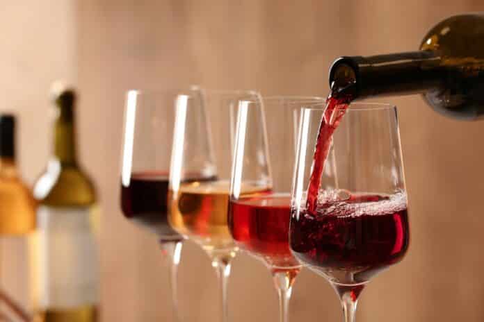 Pouring wine from bottle into glass on blurred background, closeup vino pfas
