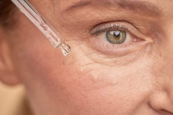 Mature woman moisturizing the skin near the eyes with a special serum PEPTIDI