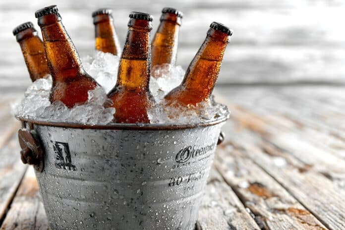 A bucket of ice filled with cold bottles of beer sits on a weathered wooden table ready to be enjoyed. BIRRA
