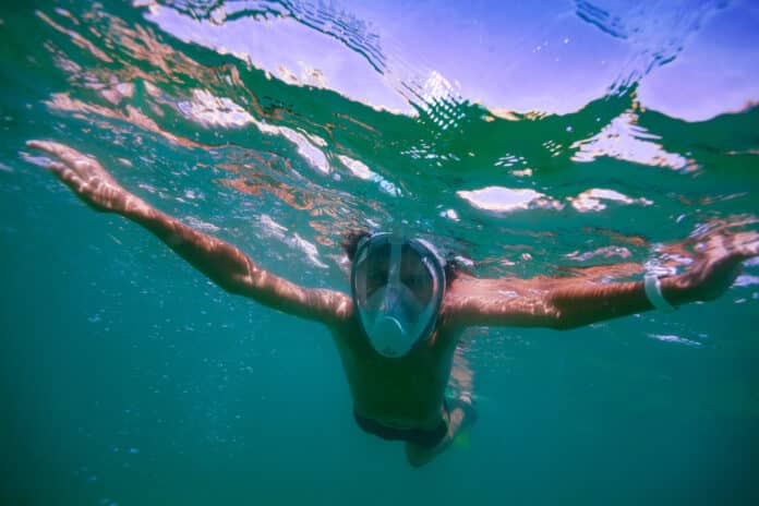 Water lover teenager dive happily among waves in full face mask