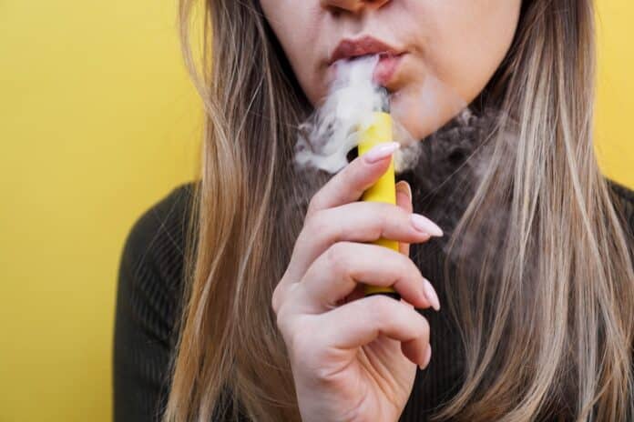 A young girl smokes disposable electronic cigarette. Bright yellow background SIGARETTE ELETTRONICHE E CIG
