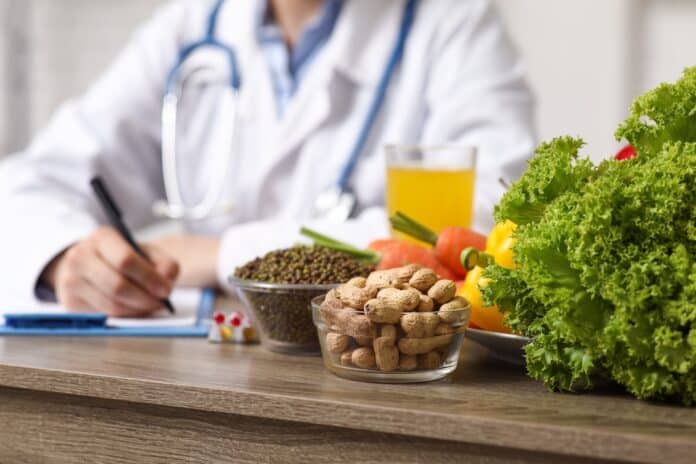 Young female nutritionist with clipboard and healthy food writing diet plan in office, closeup dieta