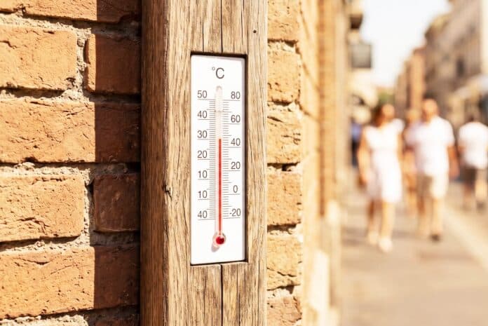 Thermometer shows high temperature on a hot summer day in a city street with blurred people and traffic, indicating extreme heat and need for cooling for commercial technology, business ONDE DI CALORE