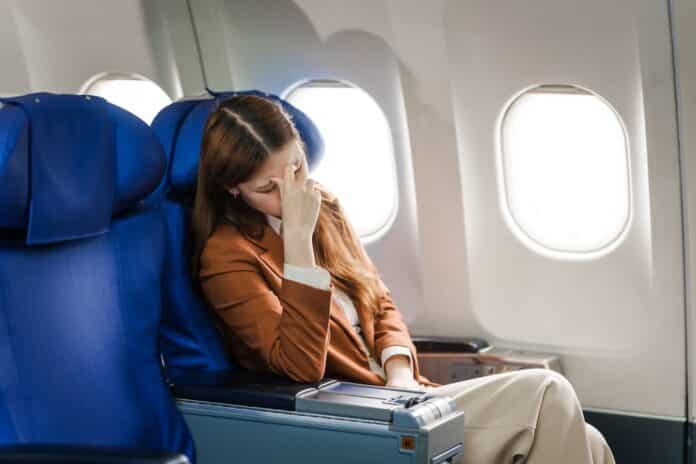 A young Asian woman is sitting in her seat as an airplane passenger, experiencing airsickness with symptoms like nausea, vomiting, dizziness, and general discomfort. jet lag