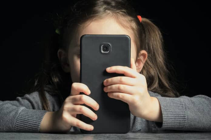 Problem of kids addiction to gadgets, online and screen time. Little girl with big smartphone in her hands META BAMBINI PROCESSO