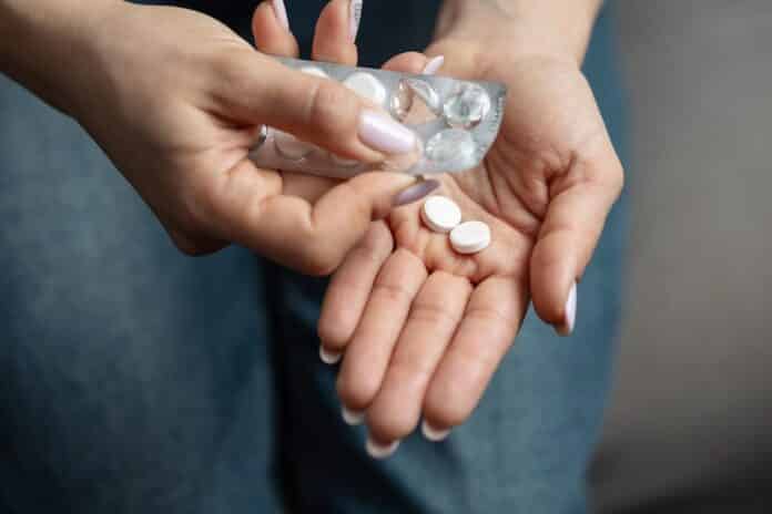 Close-up of female hands taking pills from blister pack with white round scored tablets, concept of pharmaceutical treatment cabergolina