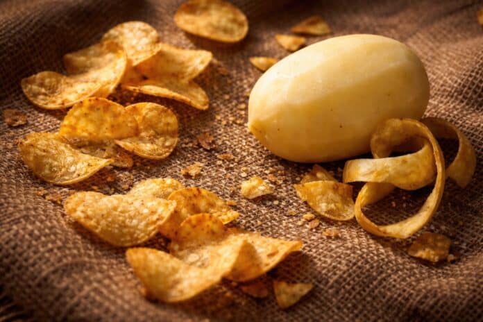 Scattered potato chips and peeled whole potato on textured burlap sack BUCCE DI PATATA CHIPS