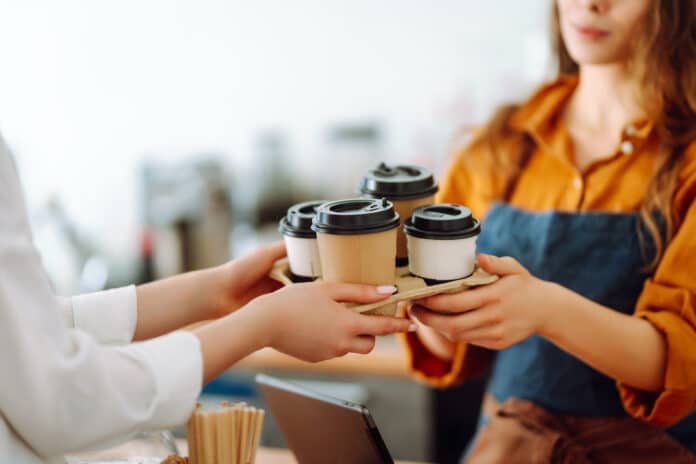 Close-up of a female barista's hands giving out a to-go drink order. The coffee shop owner gives orders to go. Takeaway drinks concept, small business. CAFFÈ FURANO