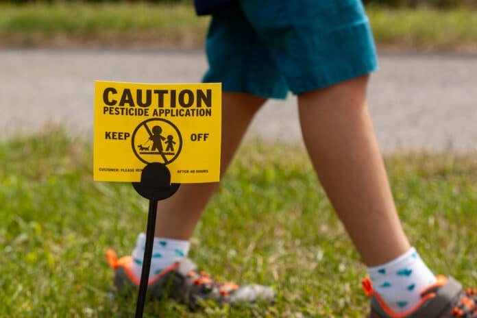 flupiradifurone bambini A yellow yard sign warning kids and pets of the recent pesticide spraying and advices them to stay away. A kid is playing regardless. Pesticide use is a big concern. flupiradifurone bambini
