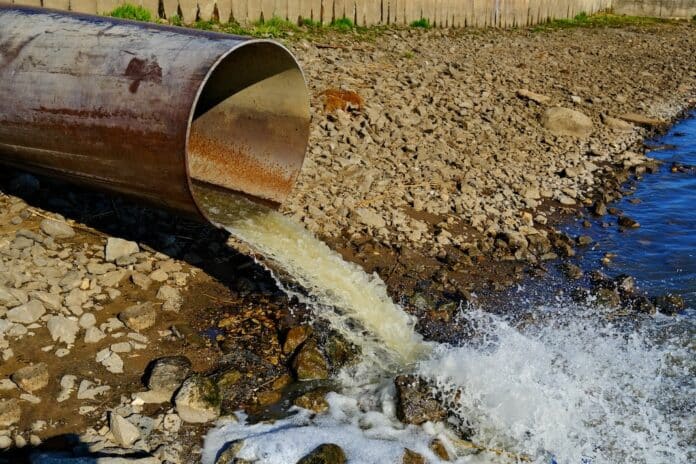 Sewage pipe discharging wastewater into river, environmental pollution, dirty water flowing from drainage outlet inquinamento pfas
